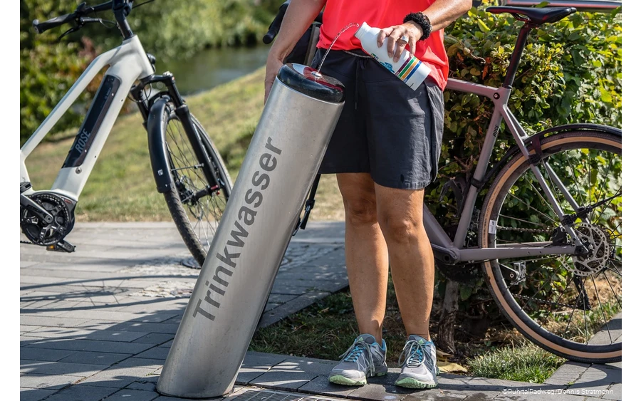 Radfahrerin füllt ihre Trinkflasche am Trinkbrunnen in Meschede mit Wasser auf