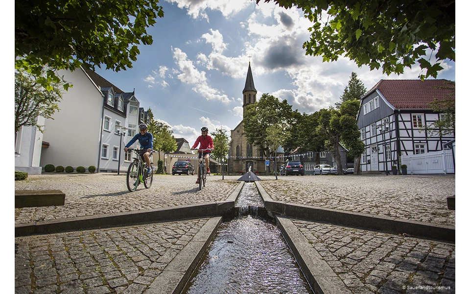 Zwei Radfahrer kommen mit ihren Fahrrädern vom Parkplatz.
