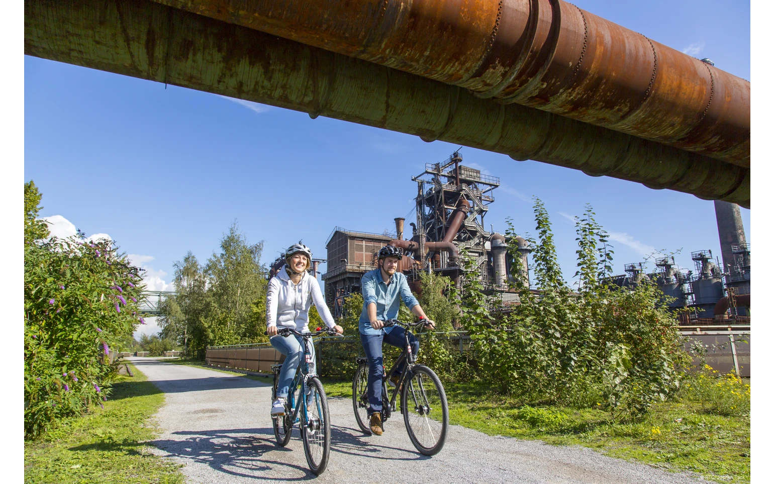 Zwei Radfahrer im Landschaftspark Duisburg bei blauem Himmel.