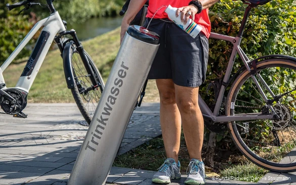 Radfahrerin füllt ihre Trinkflasche am Trinkbrunnen in Meschede mit Wasser auf