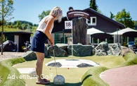 Eine Frau schlägt einen Golfball in Richtung Loch, welches sich auf einem Hügel mit dem Aussehen eines Fußballs befindet.