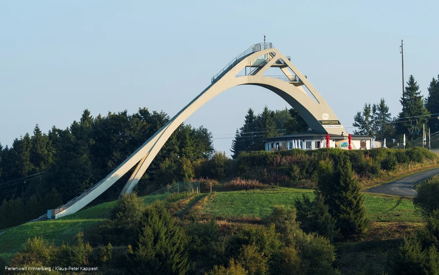 Die St. Georg Sprungschanze mit dem Restaurant "Die Schanze" umgeben von Wiesen und Wäldern.