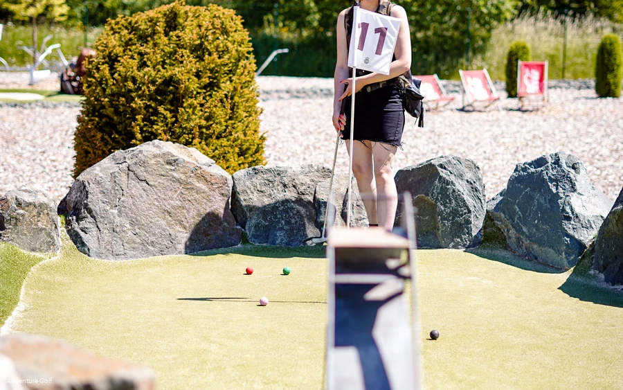 Eine Frau spielt Golf auf einer Bahn mit der St. Georg-Schanze als Hindernis.
