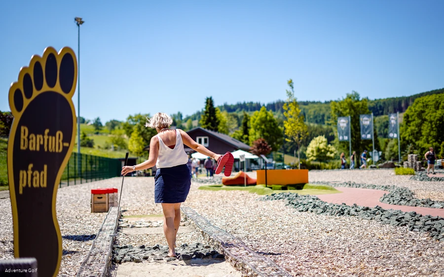 Eine Frau geht über einen Barfußpfad mit verschiedenen Untergründen.