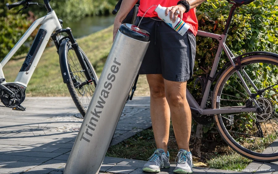 Radfahrerin füllt ihre Trinkflasche am Trinkbrunnen in Meschede mit Wasser auf
