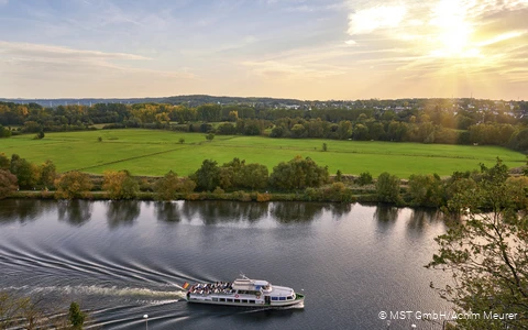 Ein Personenschiff fährt auf der Ruhr und die grünen Ruhrauen im Hintergrund.