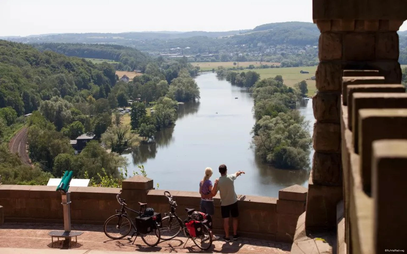 Eine Frau und ein Mann mit Rädern schauen von oben auf das Wasser
