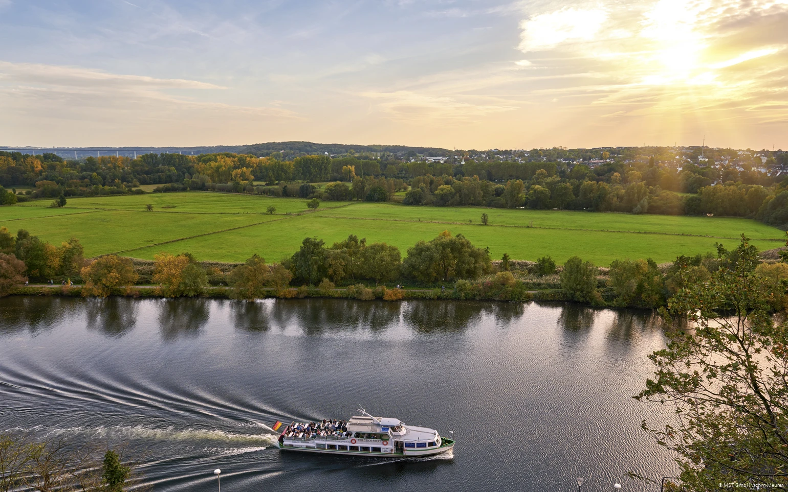 Ein Personenschiff fährt auf der Ruhr und die grünen Ruhrauen im Hintergrund.