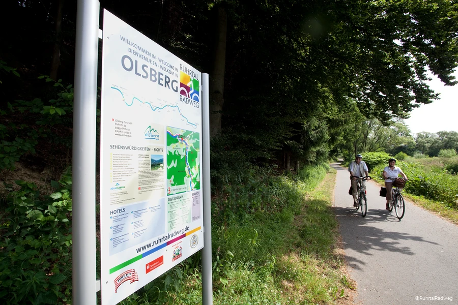 Stadtinformationsschild in Olsberg auf dem RuhrtalRadweg, an dem ein Paar auf Fahrr&auml;dern vorbei f&auml;hrt