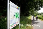 Stadtinformationsschild in Olsberg auf dem RuhrtalRadweg, an dem ein Paar auf Fahrrädern vorbei fährt