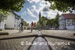 Zwei Radfahrer kommen mit ihren Fahrrädern vom Parkplatz.